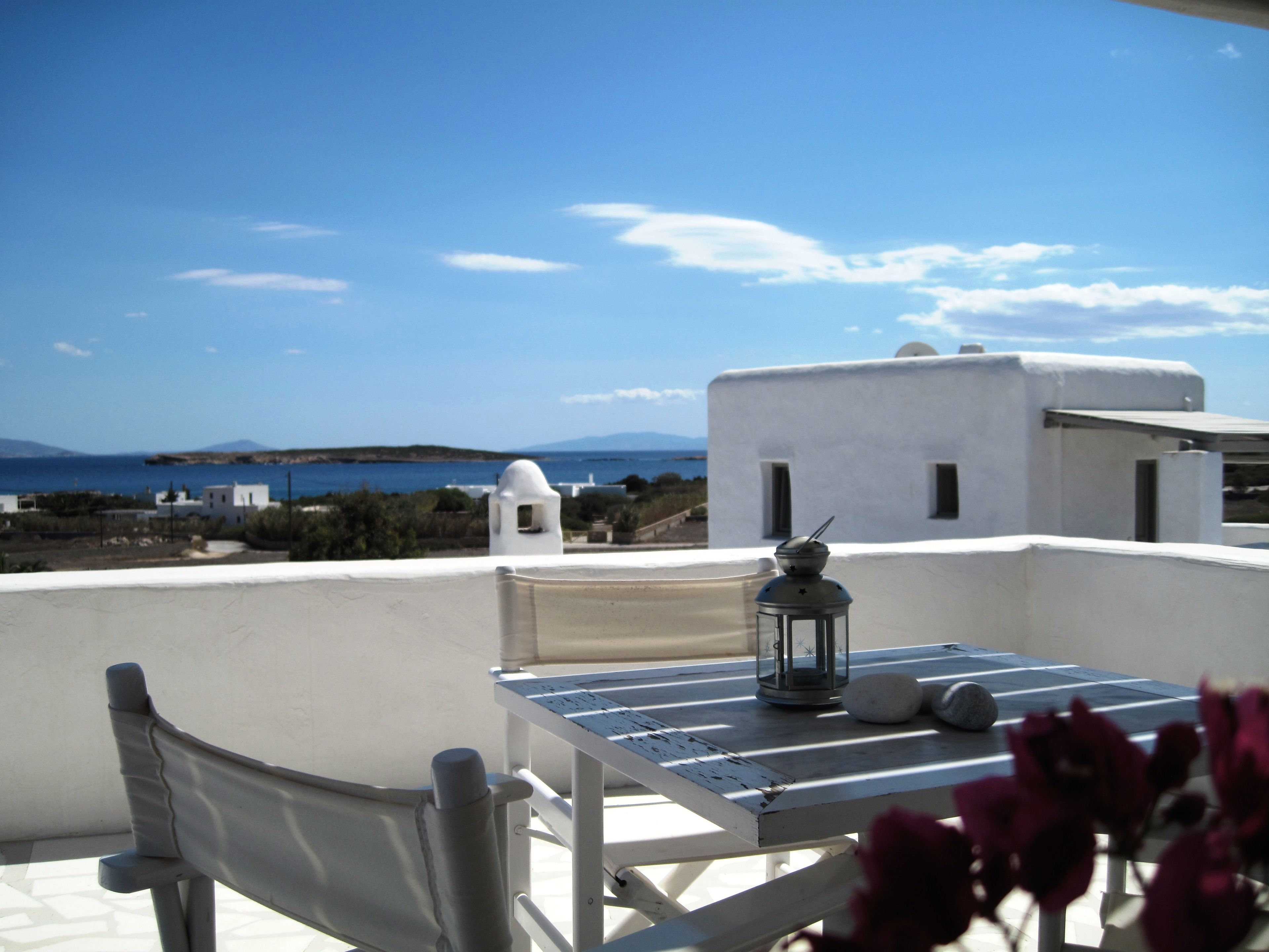 Una terraza con mesa y silla, un farol y vistas al mar y tierra a lo lejos.