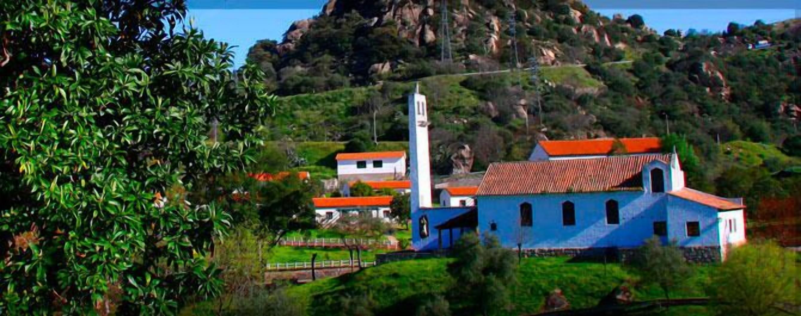 Una iglesia rural con un campanario, rodeada de vegetación y colinas.