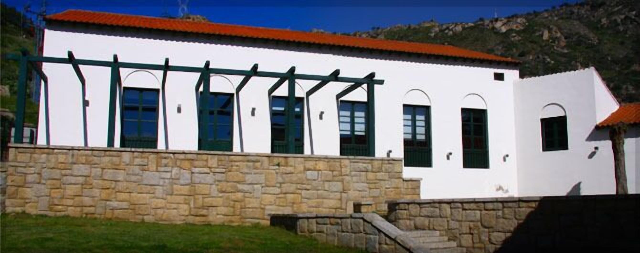 A white building with a stone wall foundation, green window frames, and a red roof.