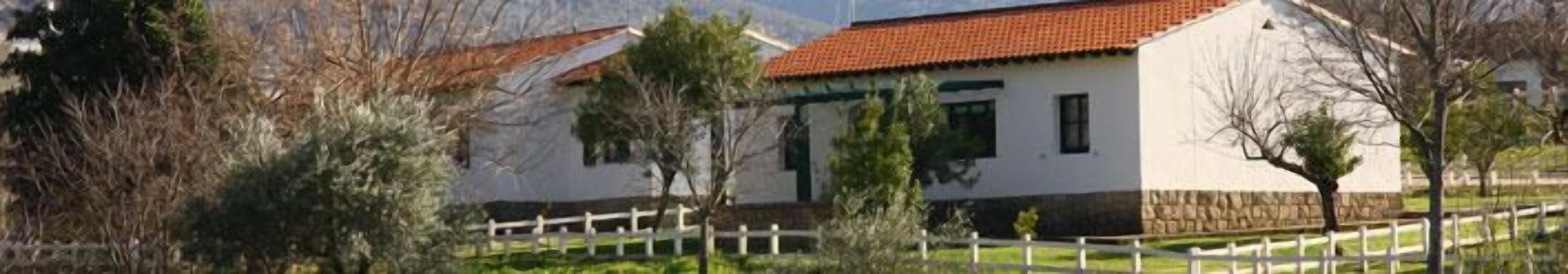 Un edificio blanco con techo rojo, rodeado por una cerca blanca y árboles.