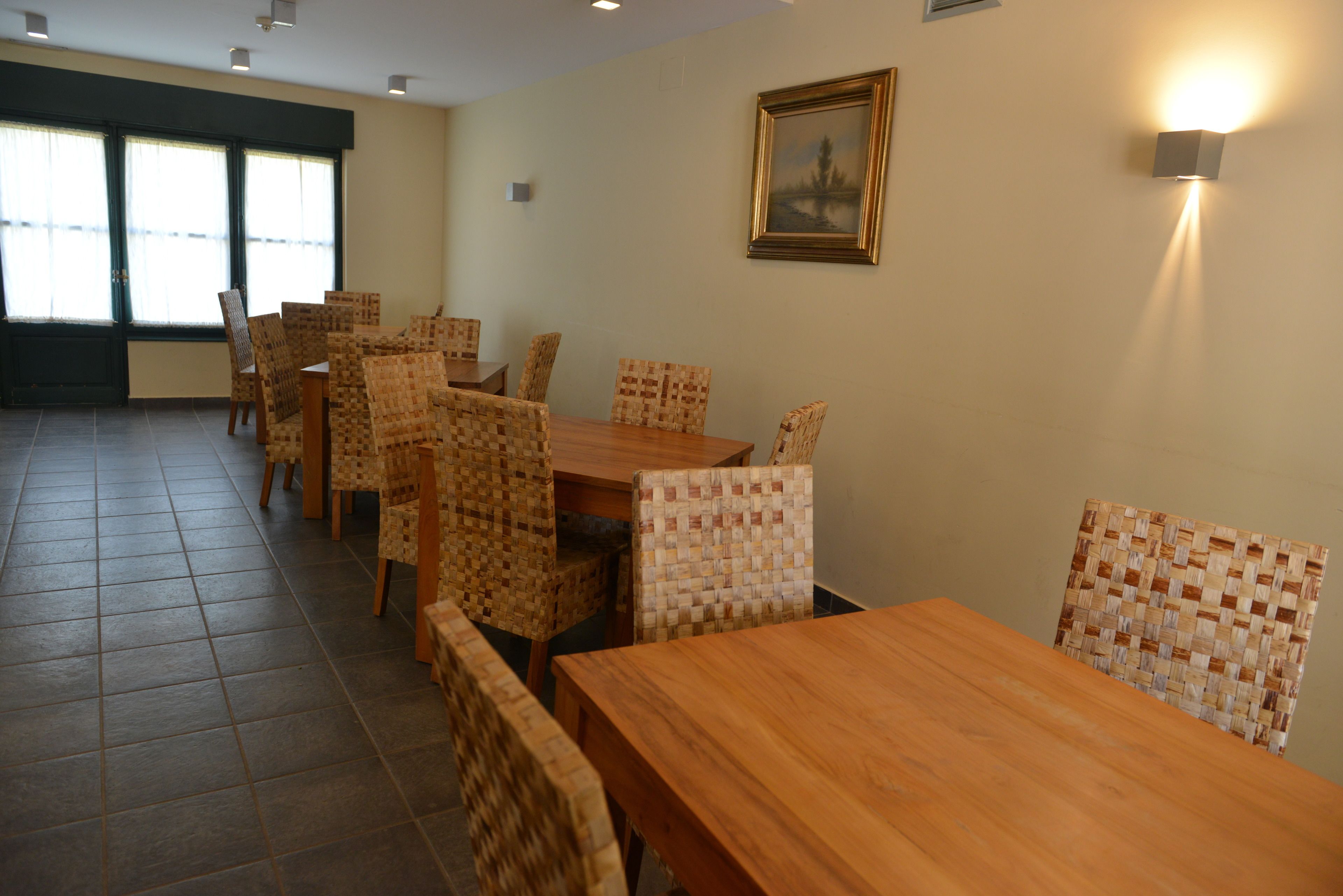 Un comedor con una mesa de madera y sillas tejidas, un cuadro en la pared y una ventana con persianas.