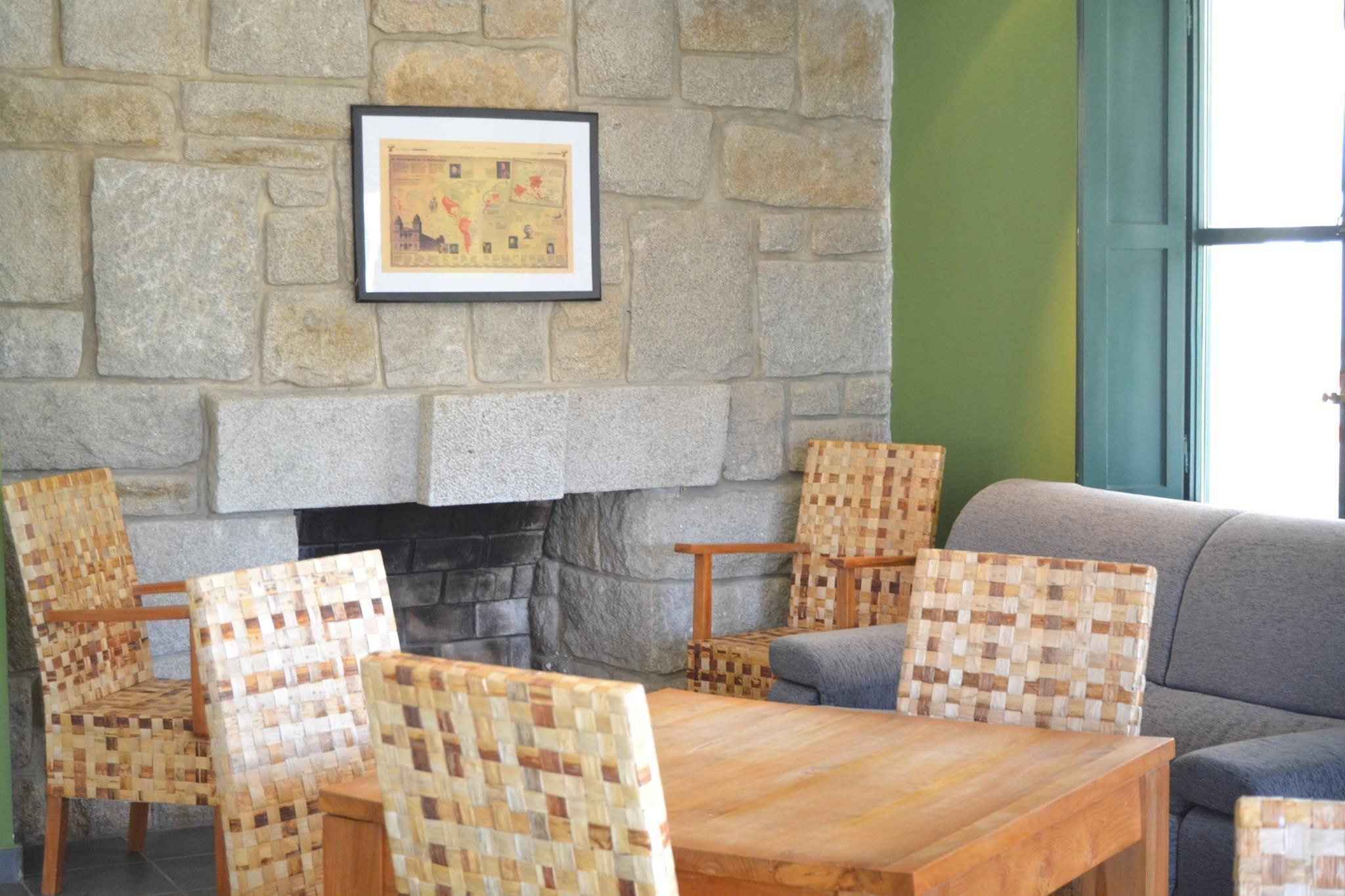 A stone fireplace with a framed map, wicker chairs, a wooden table, and a grey sofa in a room with green walls.