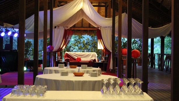 Een binneneventruimte met gedekte tafels voor een receptie, bedekt met witte stof, en een podium met verlichting op de achtergrond.