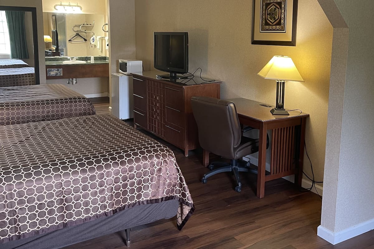 Une chambre d’hôtel avec deux lits, un bureau avec un ordinateur, une télévision et une lampe de bureau.
