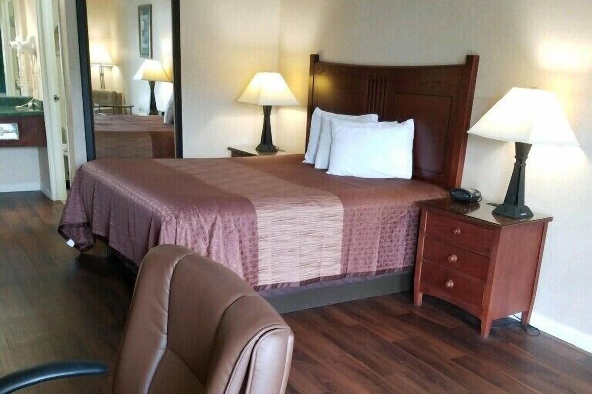Une chambre d’hôtel avec un grand lit, deux lampes de chevet, une table de chevet en bois, une chaise et un miroir.