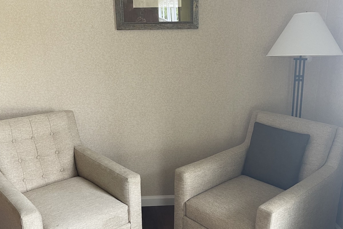 Deux fauteuils recouverts d’un tissu texturé, une œuvre d’art abstraite encadrée accrochée au mur et une lampe sur pied.