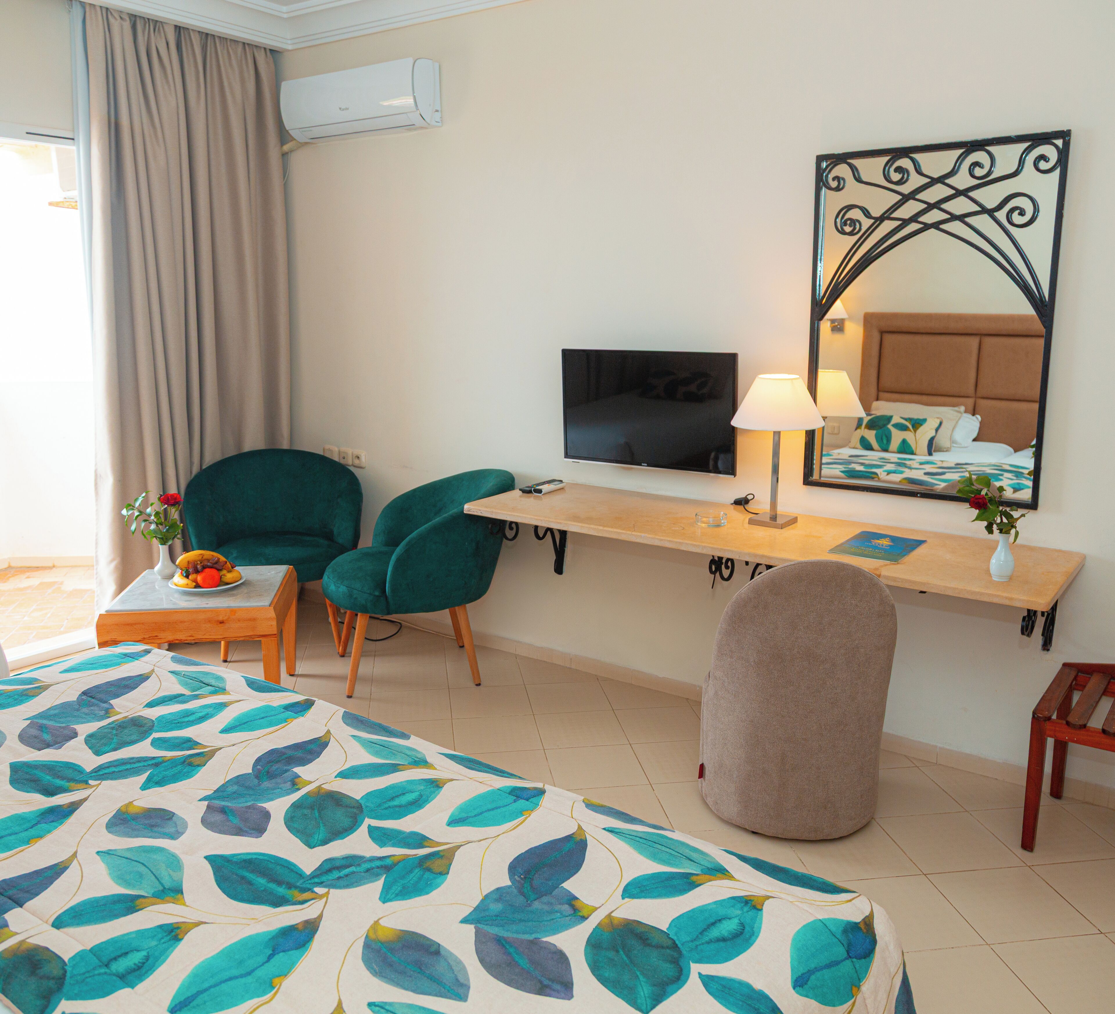 Una habitación de hotel con cama, escritorio con televisor, lámpara y dos sillas.