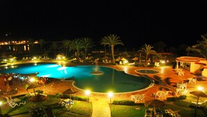 A nighttime view of a resort pool area with multiple pools, lounge chairs, and umbrellas. - Itropika Hôtel (Tabarka)