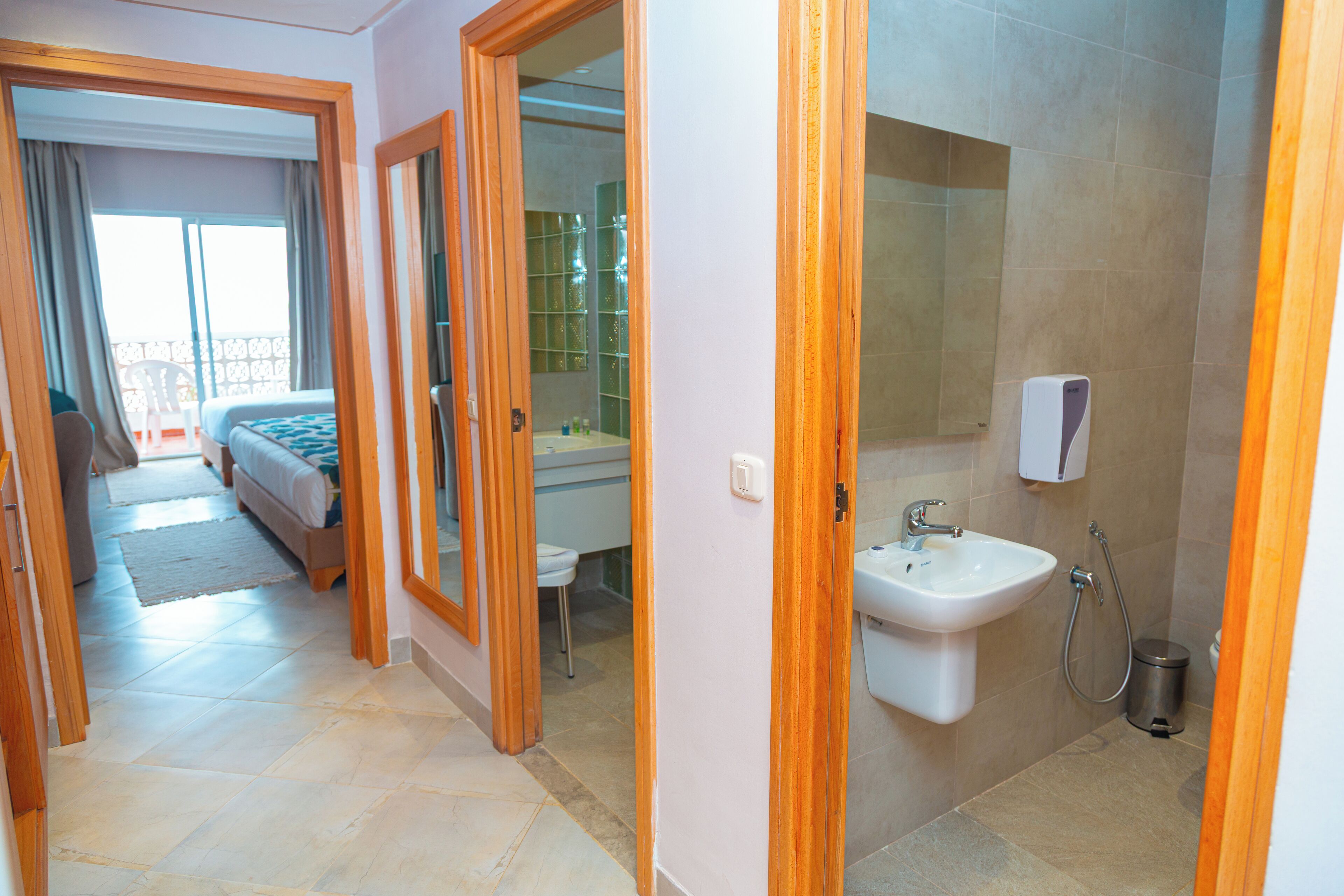 A hotel room with a bed, a bathroom with a sink and shower, and a balcony with a chair.