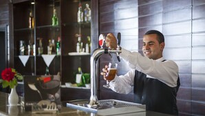 A barista pouring a drink into a glass at a bar with a polished countertop and a display of various bottles in the background. - Itropika Hôtel (Tabarka)