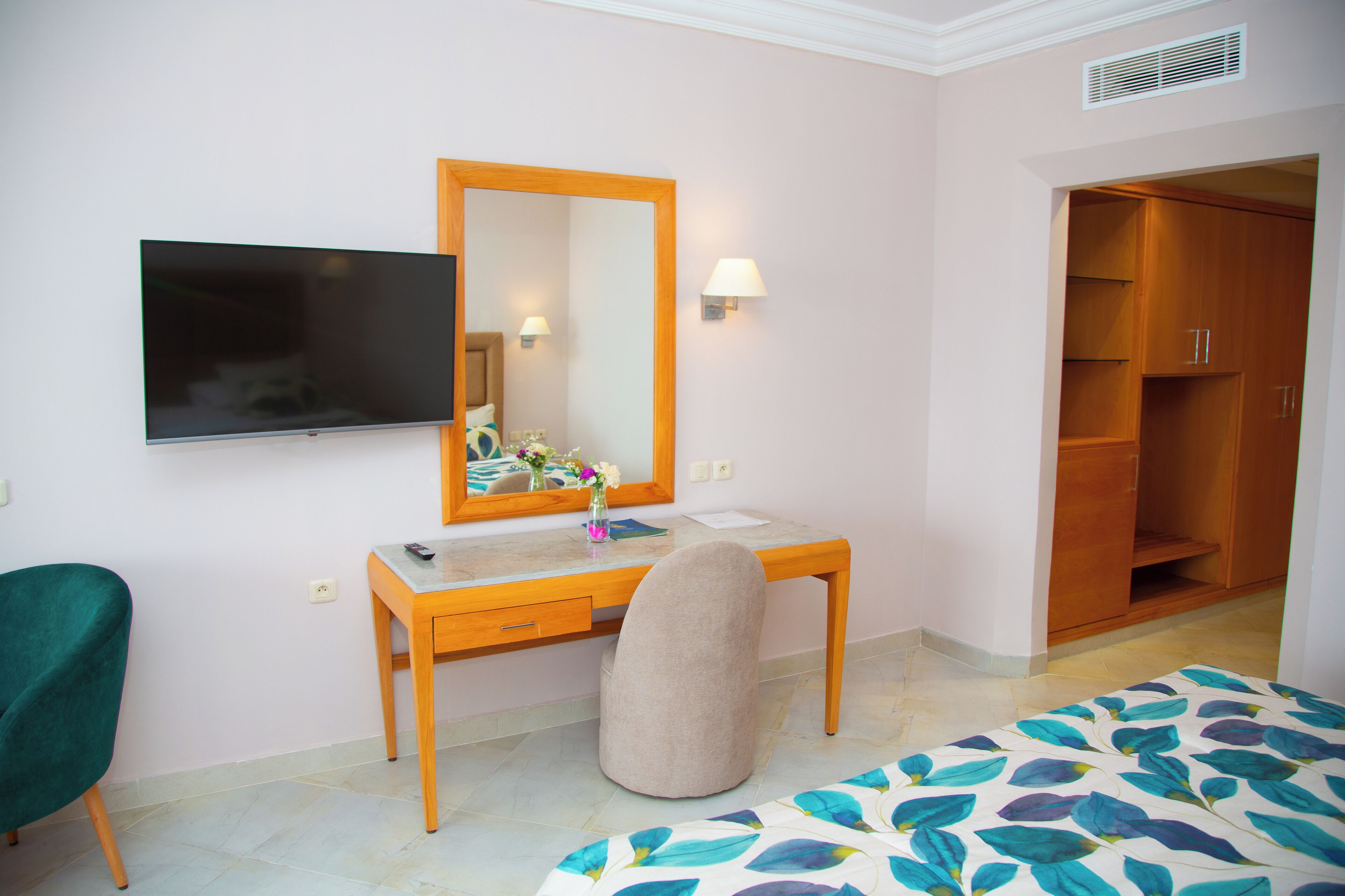 Una habitación de hotel con un escritorio de madera, una silla, una cama con colcha estampada, un televisor en la pared y un armario.