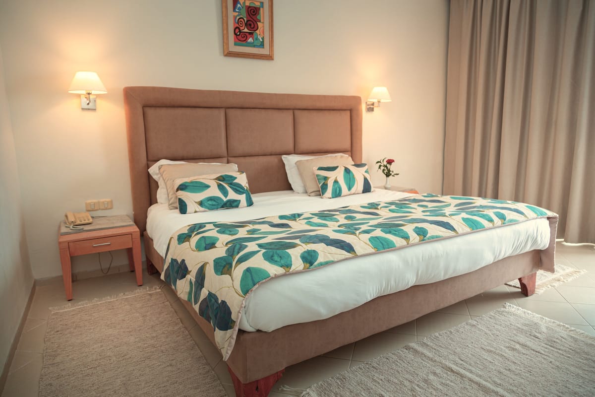 A neatly made bed with a floral bedspread, a wooden nightstand with a telephone, and two wall-mounted lamps.