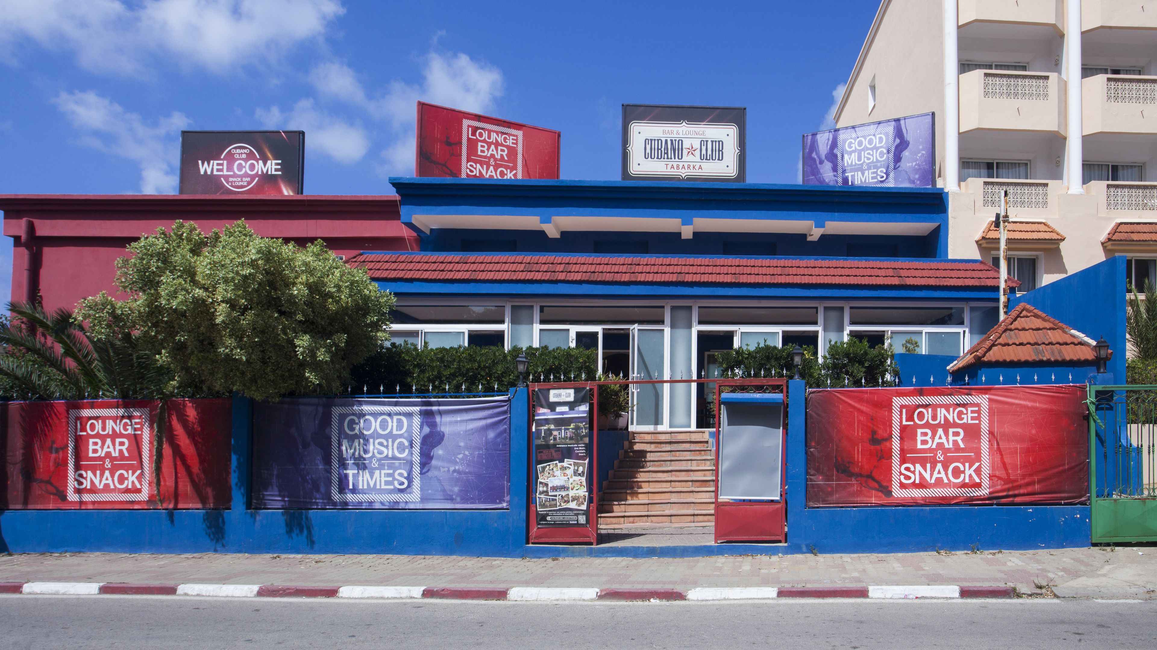 A building with multiple signs advertising a lounge bar and snack, a welcome sign, and a bar & lounge tabarka.
