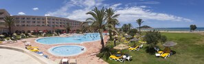 Ett semesterhotell med en stor pool, solstolar och utsikt över stranden.
