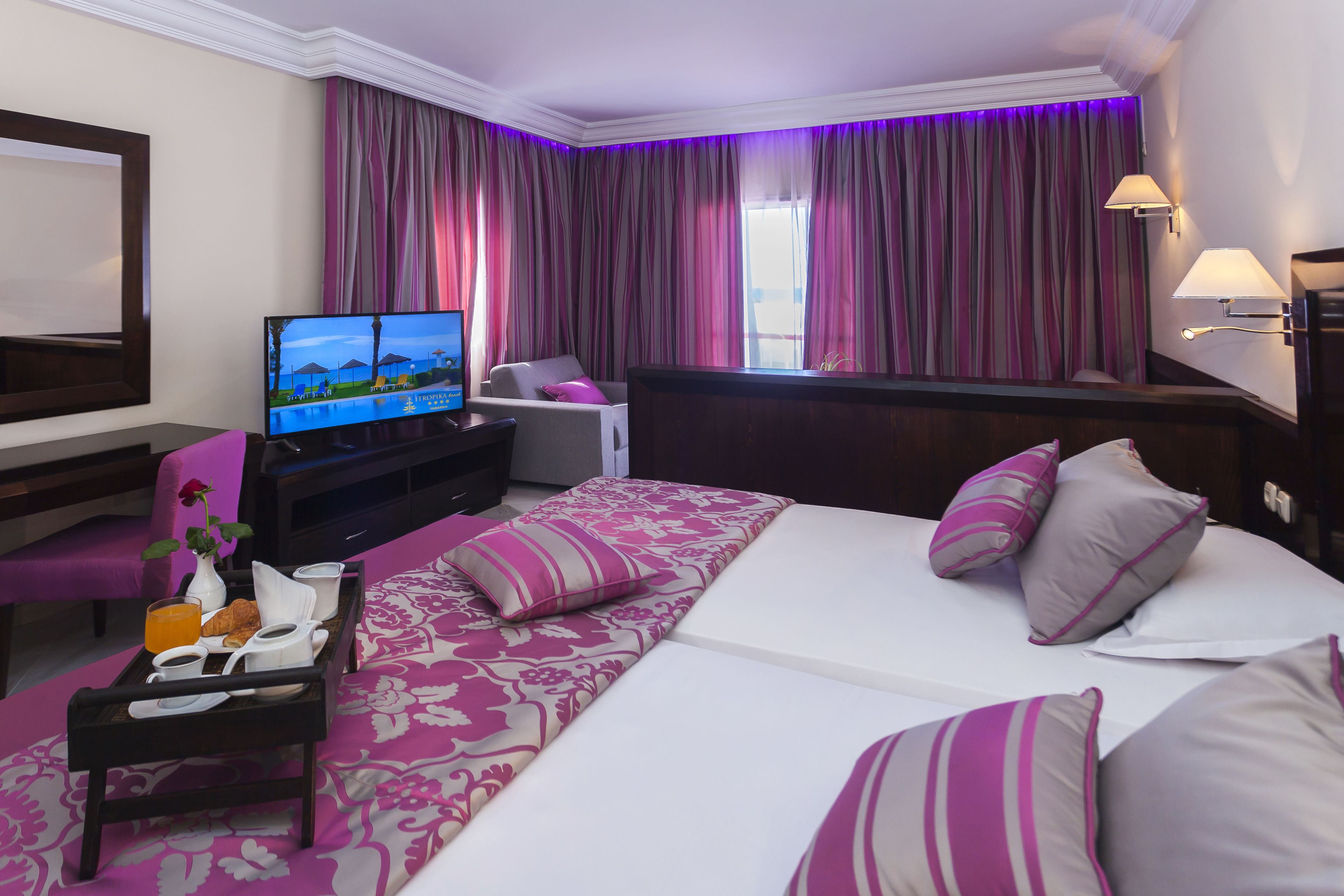 Habitación de hotel con cama, televisión, escritorio y bandeja de desayuno, además de una ventana con cortinas.