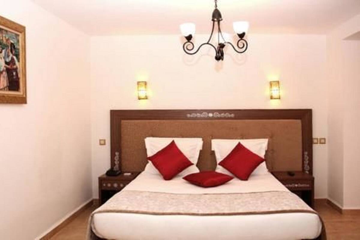 Ein ordentlich eingerichtetes Hotelzimmer mit einem großen Bett, zwei Nachttischen, einer Kandelaber und einem Gemälde an der Wand.