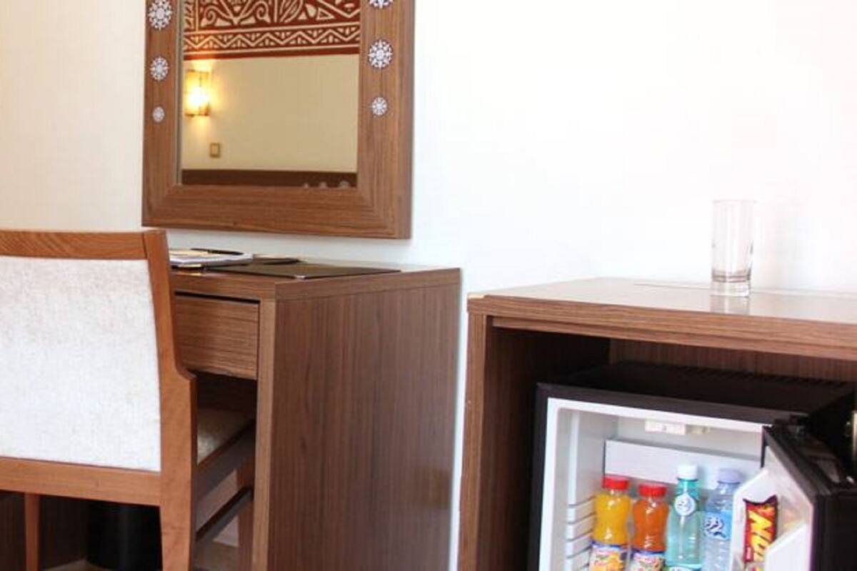Ein Hotelzimmer mit einem Bett, einem Holztisch mit Stuhl, einem Fernseher, einem Spiegel und einer Minibar mit Getränken.