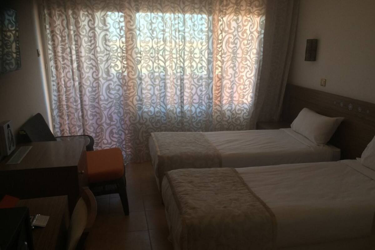 Ein Hotelzimmer mit zwei Betten, einem Schreibtisch, einem Stuhl und einem Vorhang mit Muster.