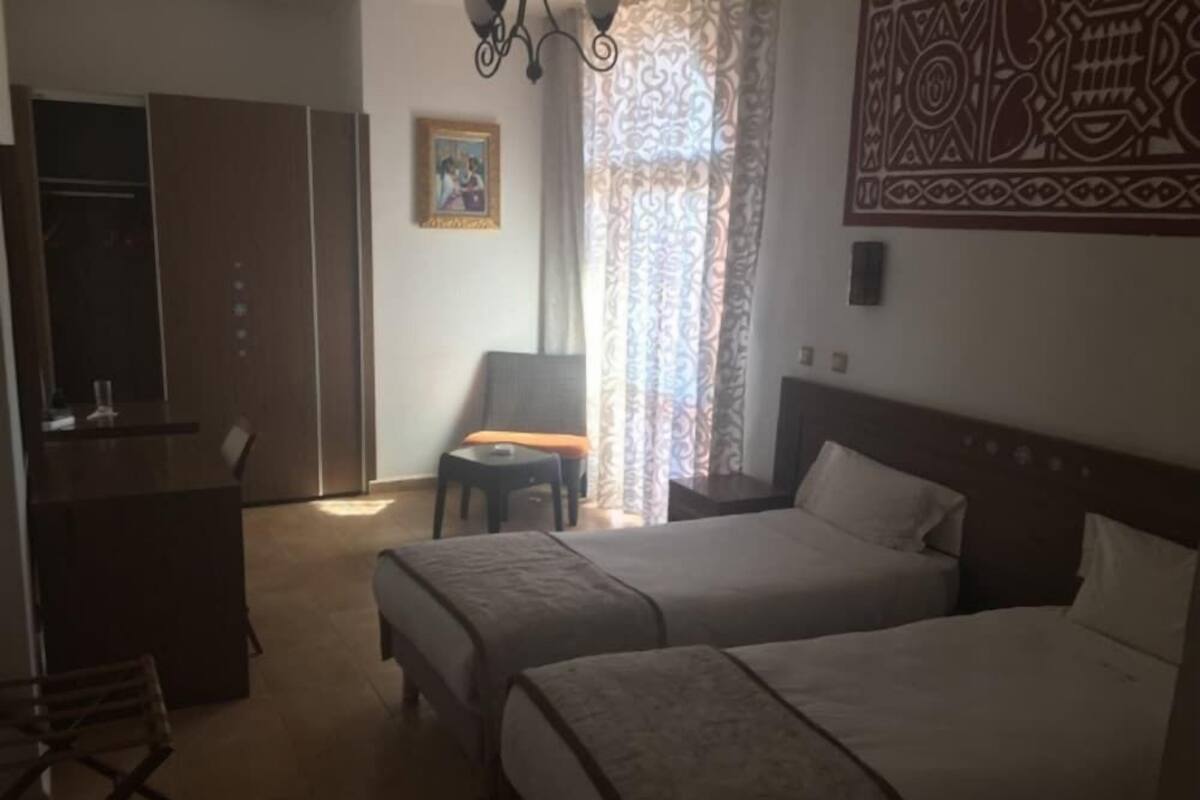 Ein Hotelzimmer mit zwei Betten, einem Schreibtisch, einem Stuhl, einem Kleiderschrank und einer Wanddekoration mit Muster.