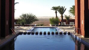 A swimming pool with a view of a desert landscape, surrounded by palm trees and lounge chairs. - Hôtel Gourara (Timimoun)