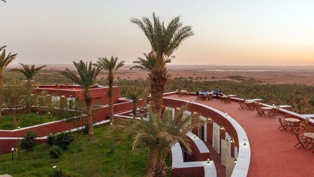 A terrace with outdoor seating, palm trees, and a view of a flat landscape. - Hôtel Gourara (Timimoun)