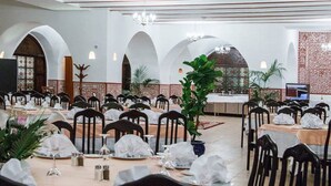 A banquet hall with multiple tables set for dining, featuring a classic architectural design with arches and a chandelier. - Hôtel Gourara (Timimoun)