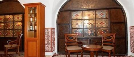 A room with a wooden cabinet, two chairs, a round table, and a large arched window with patterned glass.