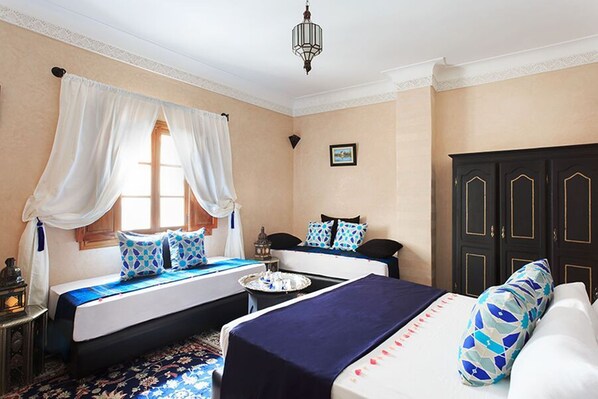 A hotel room with two beds, a small table, a wardrobe, and a window with curtains.
