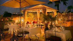 An outdoor dining area with tables set under large umbrellas, surrounded by plants and lanterns. - Arabian Riad (Marrakech)