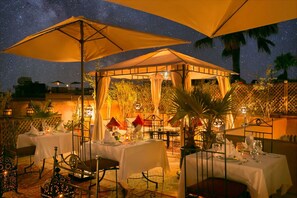An outdoor dining area with tables set under large umbrellas, surrounded by plants and lanterns. - Arabian Riad (Marrakech)