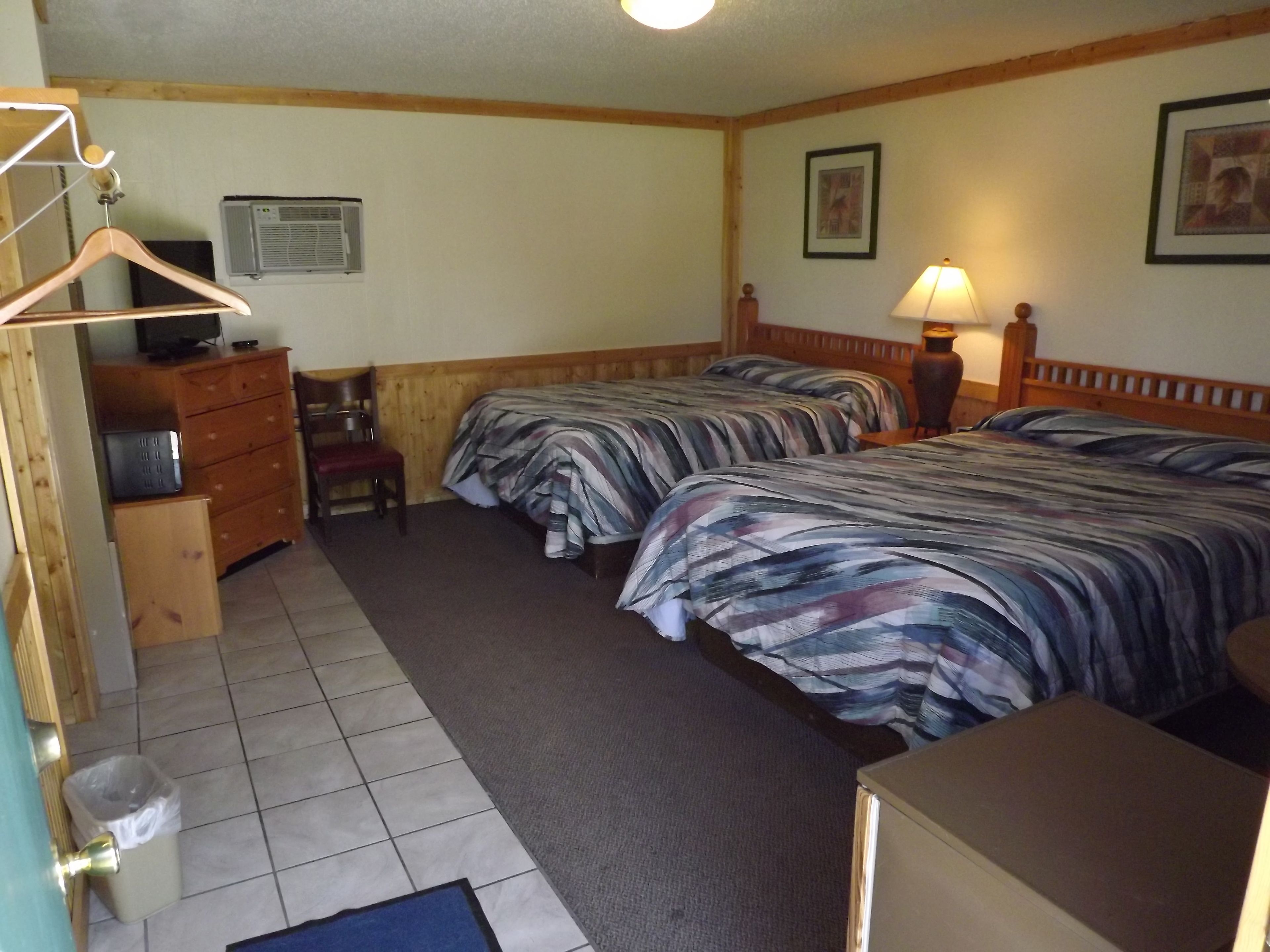 A hotel room with two beds, a dresser, a chair, a desk, and a television.