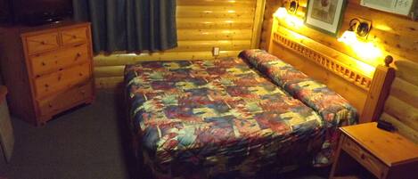 A cozy log cabin room with a bed, dresser, and a television.