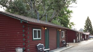 Une rangée de cabanes en rondins, avec des bordures vertes et des bancs en métal à l’extérieur.