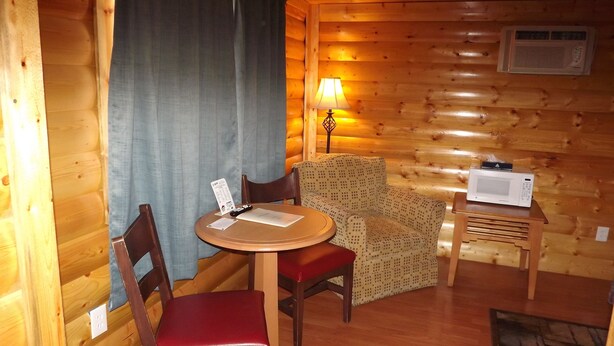 L’intérieur chaleureux d’un chalet, avec un revêtement mural en bois, une table à manger entourée de chaises, un canapé à motifs, une petite table d’appoint avec un micro-ondes et une lampe.