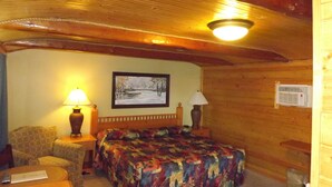 Une pièce confortable avec un lit, deux lampes, un tableau, un plafond en bois et une petite table.