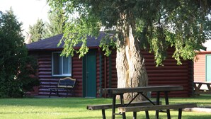 Une cabane en rondins avec une porte verte, un banc et une table de pique-nique devant.