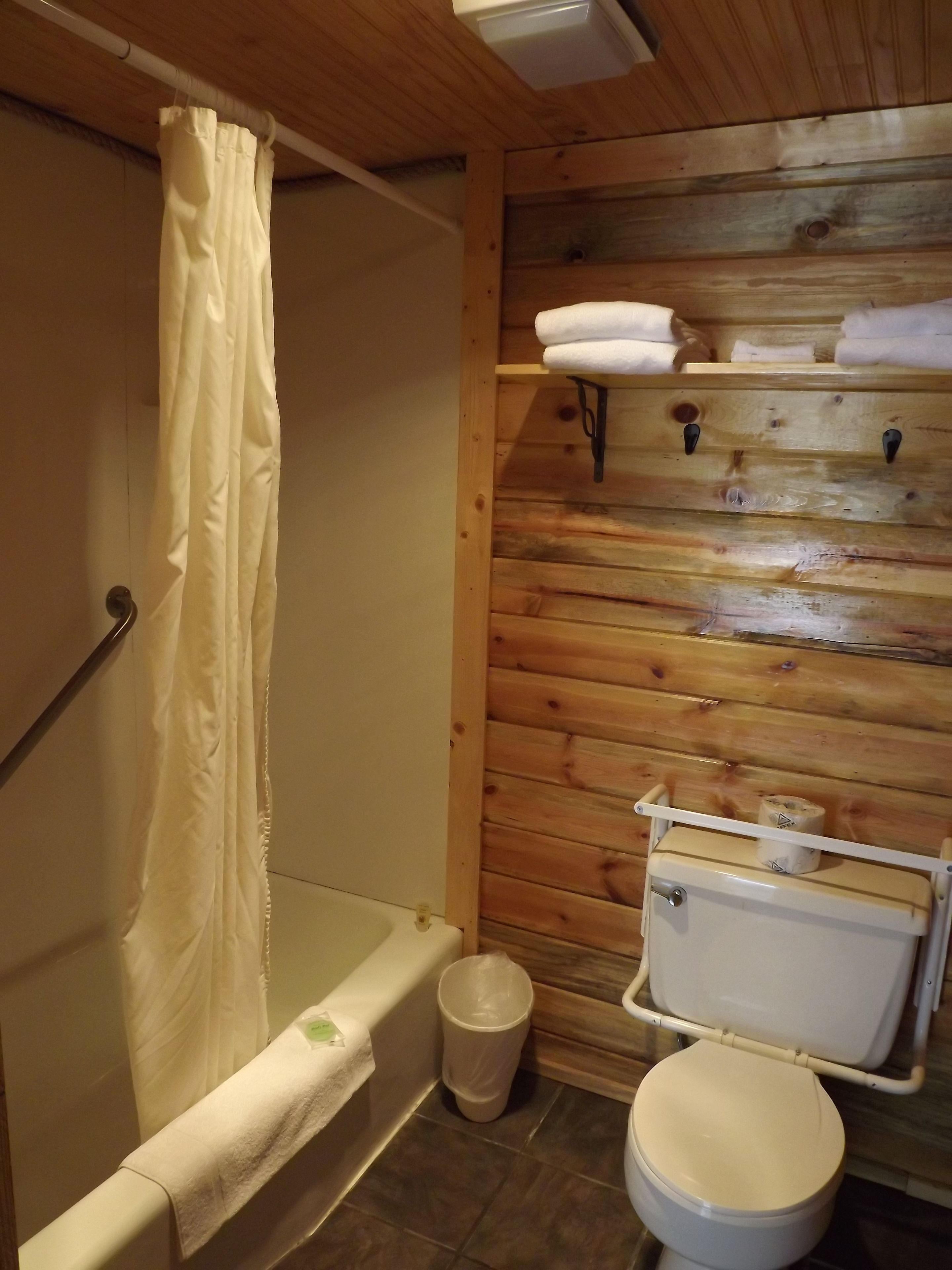 A bathroom with a wooden wall, a bathtub, a toilet, and a shower curtain.