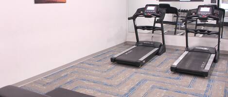 Un gimnasio con cintas de correr, bancos y una amplia pantalla de televisión.