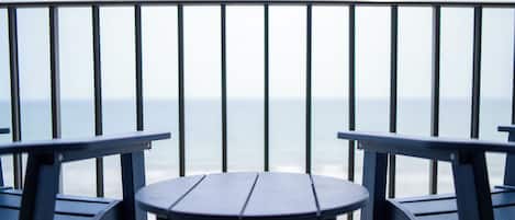 A balcony with a view of the ocean, featuring two chairs and a small table.