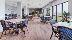 A spacious dining area with high ceilings, large windows, and a view of the outdoors. - Crystal Coast Oceanfront Hotel (Atlantic Beach)