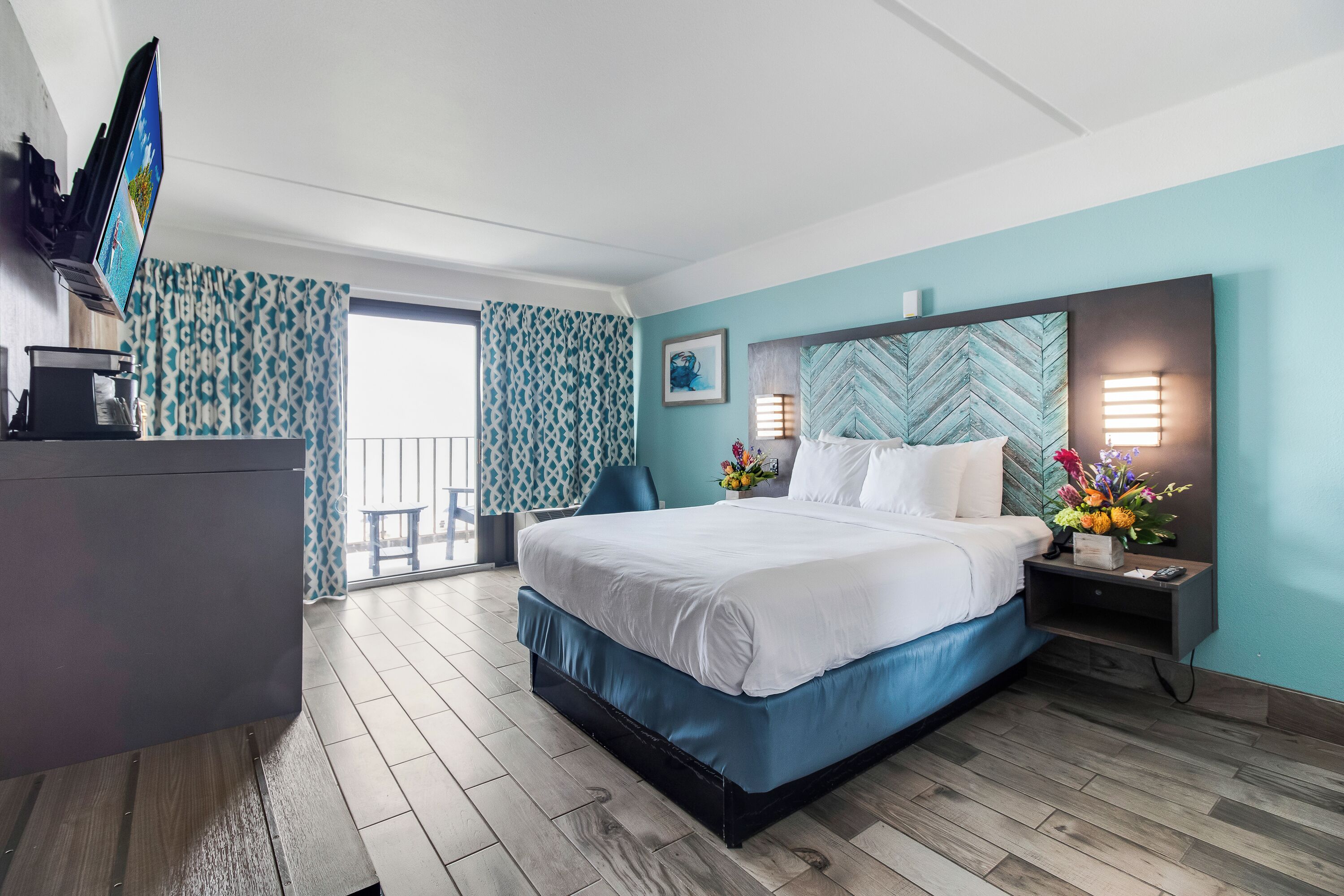 Une chambre d’hôtel avec un lit, un bureau, une télévision, une table de chevet et une fenêtre avec des rideaux.