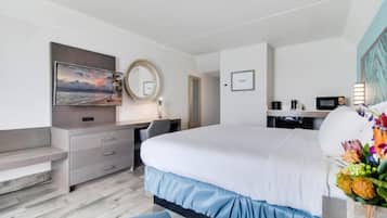 Habitació d'hotel amb un llit, una taula de treball, una cadira, un televisor, un mirall i un arranjament floral.