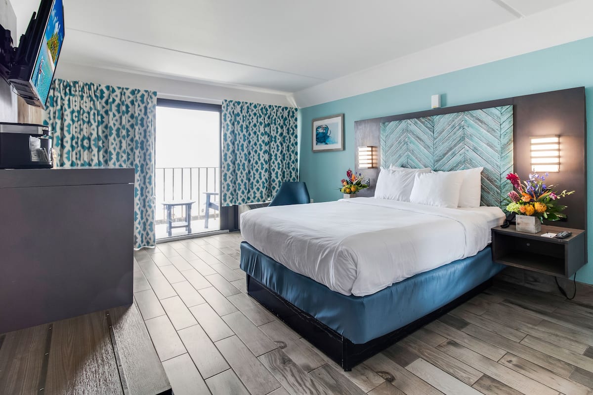 Ein Hotelzimmer mit Bett, Schreibtisch, Fernseher und Balkon mit gemusterten Vorhängen.