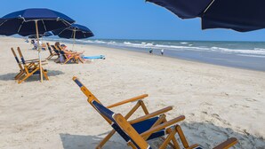 A beach with rows of beach chairs and umbrellas, a clear sky, and the ocean in the background. - Crystal Coast Oceanfront Hotel (Atlantic Beach)