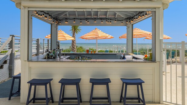 A seaside bar with three stools, a counter, and striped umbrellas. - Crystal Coast Oceanfront Hotel (Atlantic Beach)