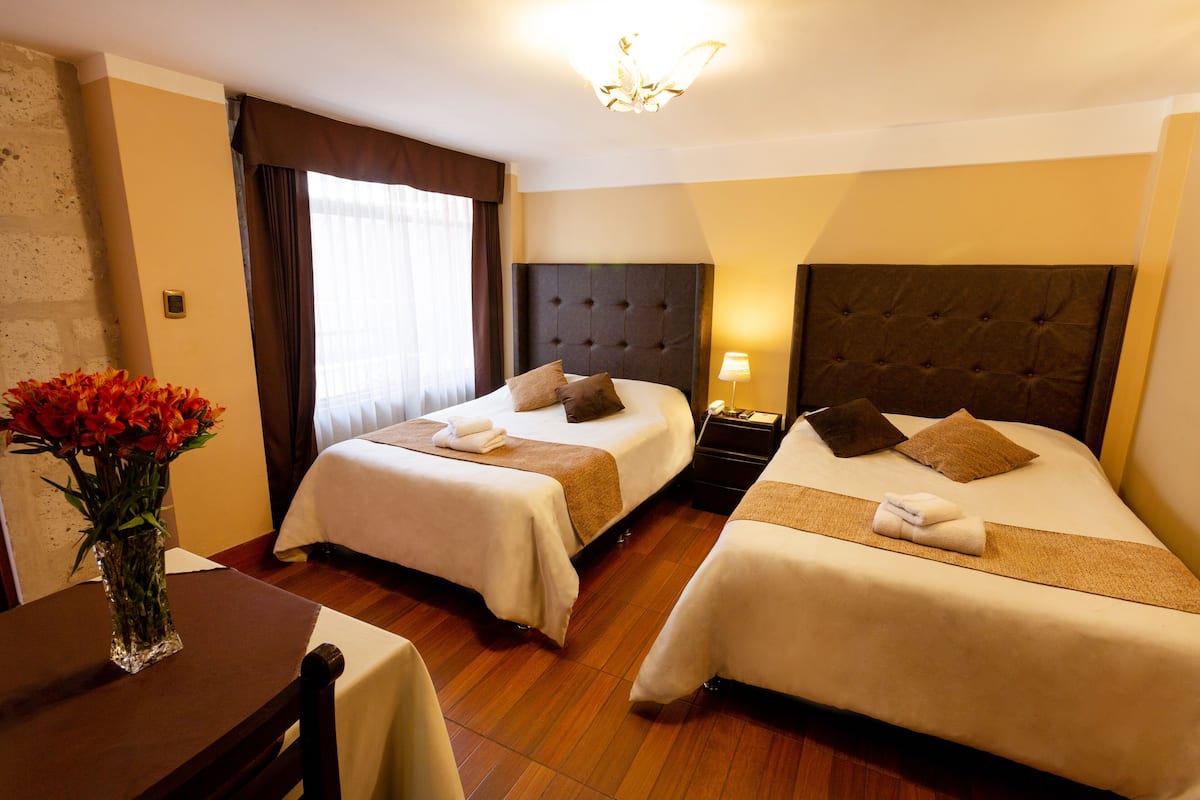 Een hotelkamer met twee bedden, een nachtkastje, een lamp, een vaas met bloemen en een houten tafeltje.