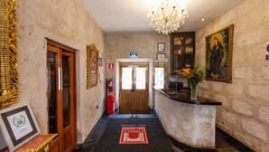 A hotel lobby with a reception desk, a chandelier, a framed picture, and a door. - El Portal de San Lázaro (Arequipa)