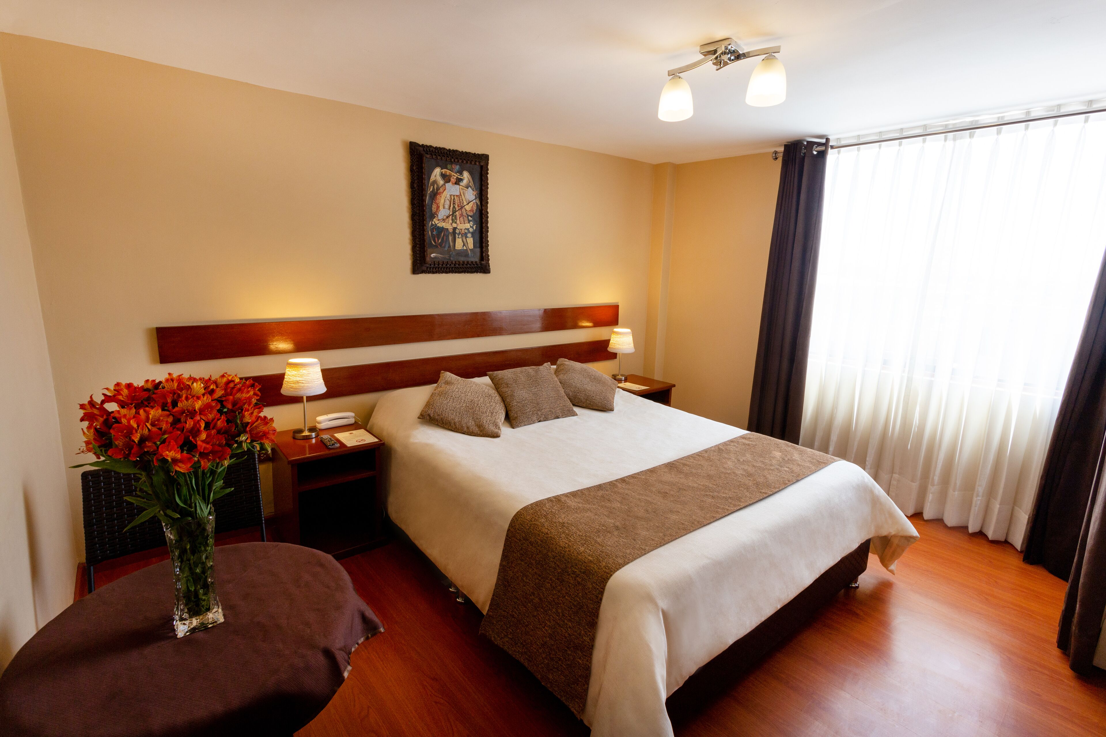 Una habitación de hotel con una cama grande, mesitas de noche, una florera y un cuadro en la pared.