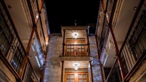 A narrow, dimly lit alleyway between buildings with wooden balconies and barred windows, leading to a brightly lit entrance. - El Portal de San Lázaro (Arequipa)