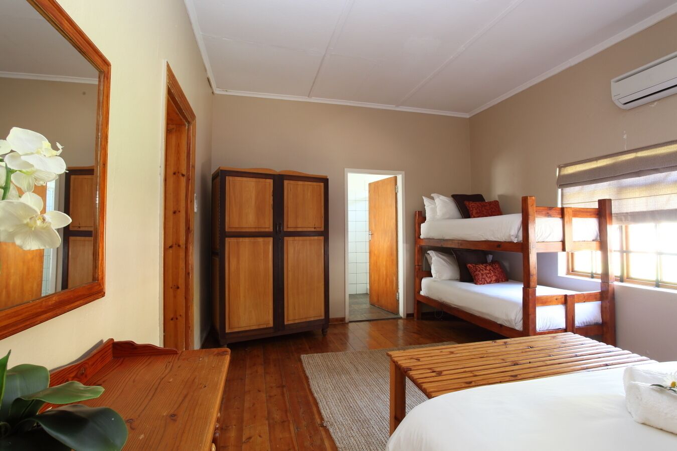 Una habitación con armario de madera, camas literas, un espejo y una ventana con persianas.